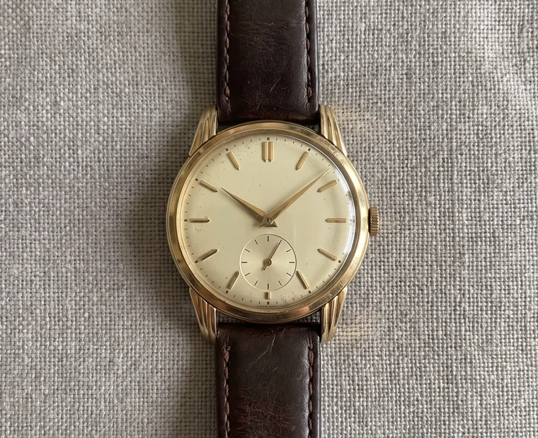 A snapshot of an old gold wristwatch on a grey table.